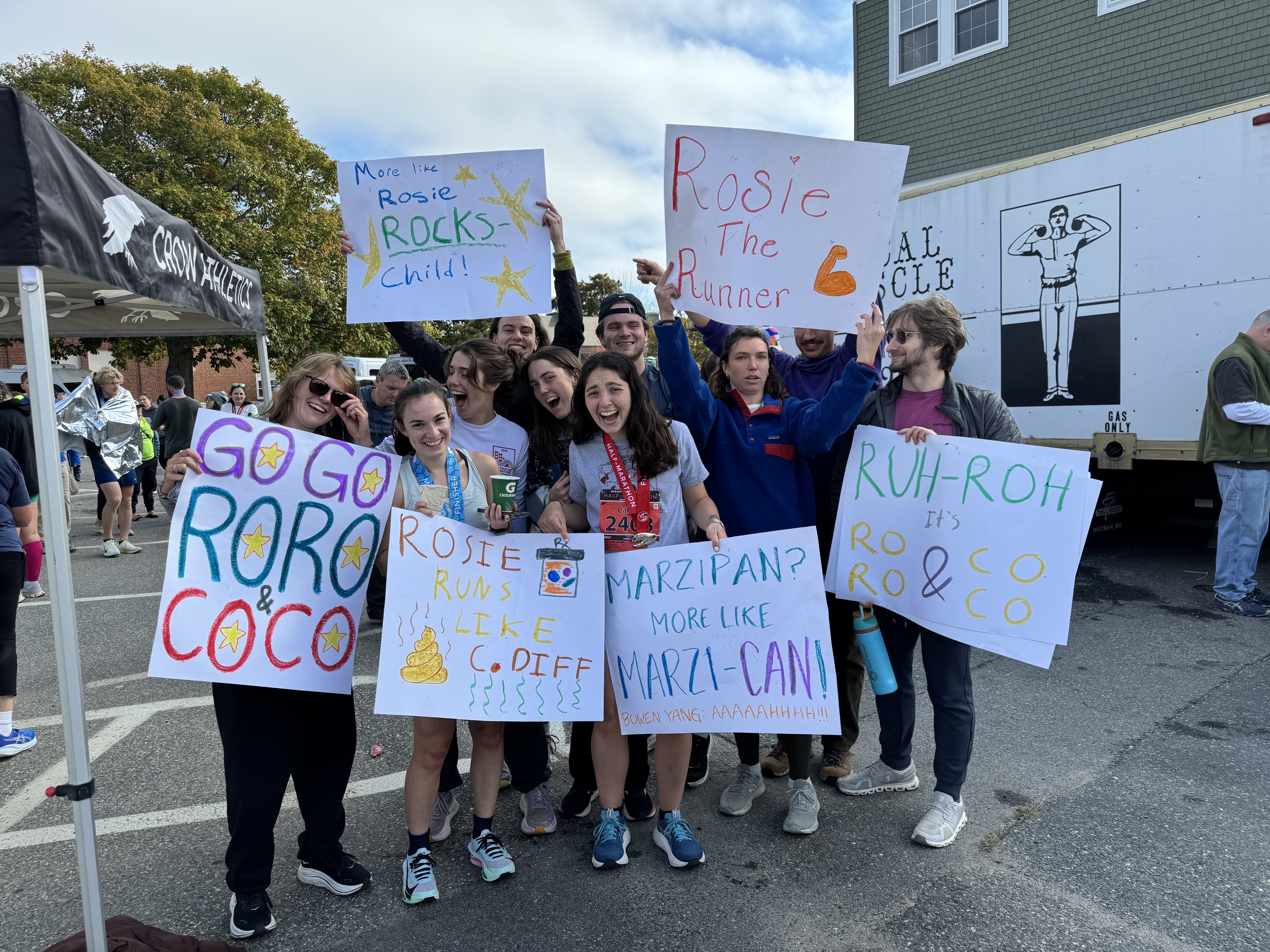 A group of friends holding handmade, funny signs cheering Rosie on at a race.